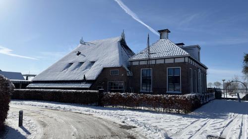 una casa con techo cubierto de nieve en PUUR Eastermar - monumentaal, authentiek en luxe koetshuis aan open vaarwater met jacuzzi en sauna, en Oostermeer
