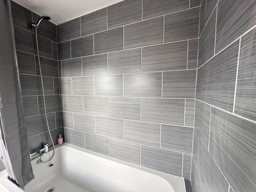 La salle de bains est pourvue d'une baignoire blanche et de carrelage gris. dans l'établissement Maddren House By Blue Skies Stays, à Middlesbrough