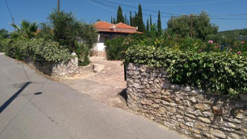 a stone wall with bushes and flowers on a street at Giannis House 2 minutes walk to the beach Peroulia in Kómboi
