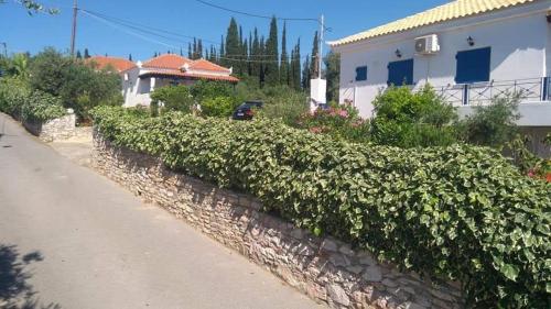 a stone retaining wall with green bushes next to a house at Giannis House 2 minutes walk to the beach Peroulia in Kómboi