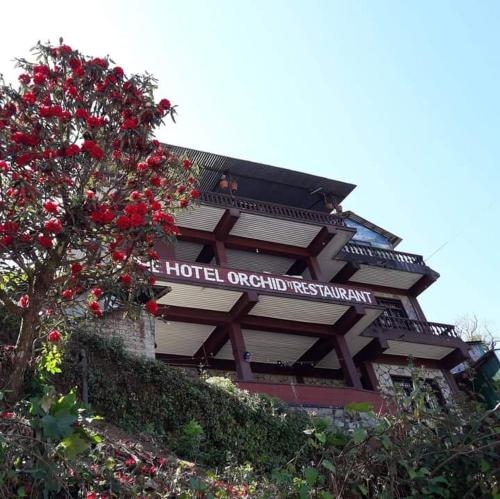 un edificio con un árbol con flores rojas delante de él en The Hotel Orchid & Restaurant, en Kāskī