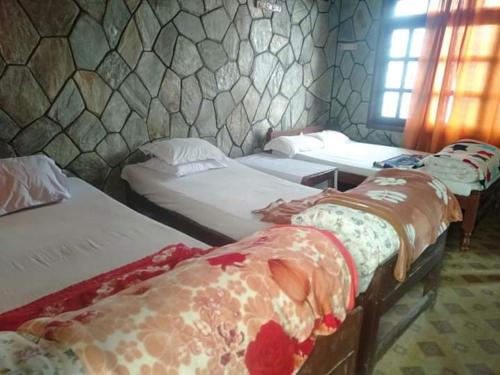 Habitación con 3 camas y pared de piedra. en The Hotel Orchid & Restaurant, en Kāskī