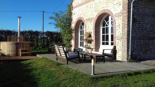 eine Terrasse mit zwei Bänken und einem Tisch vor einem Backsteingebäude in der Unterkunft La grange d'Armand in Mentheville