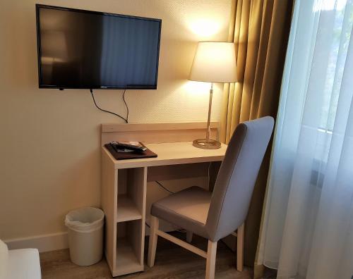 a desk with a chair and a television on a wall at ParkHotel Bad Harzburg in Bad Harzburg