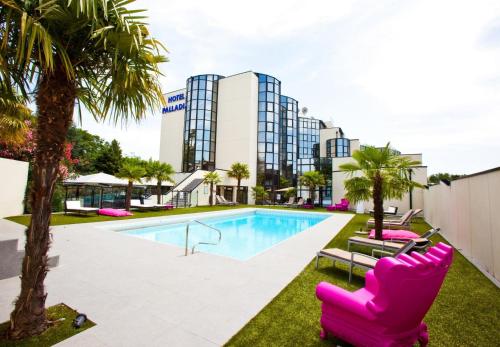 a pool with pink chairs and palm trees in front of a building at Hotel Palladia in Toulouse