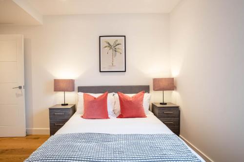 um quarto com uma cama com almofadas vermelhas e 2 candeeiros em Deluxe & Chic 1 & 2 Bed Apts near Heathrow, Legoland, & Windsor Slough em Slough