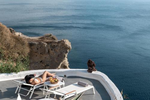 a woman laying in a chair next to the ocean at Diamond Luxury Suites Collection in Oia