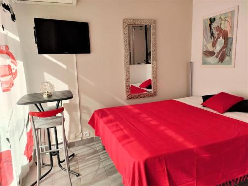 - une chambre avec un lit rouge, une table et un miroir dans l'établissement Studio 411, Héliopolis AB au village naturiste, au Cap d'Agde