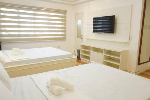 a white bedroom with two beds and a flat screen tv at Makati Altean Apartment (Leonora Room) in Manila