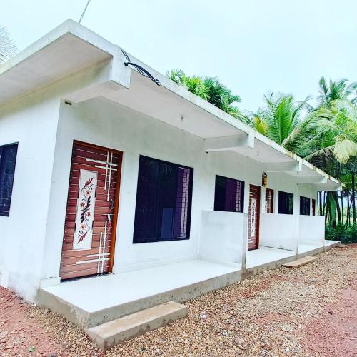 a white building with two doors and palm trees at Makayla Farm Stay in Pernem
