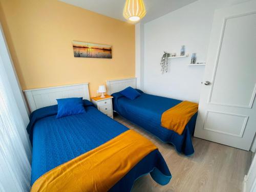 1 dormitorio con 2 camas con sábanas azules y naranjas en Apartamento primera linea de playa Valdelagrana, en El Puerto de Santa María
