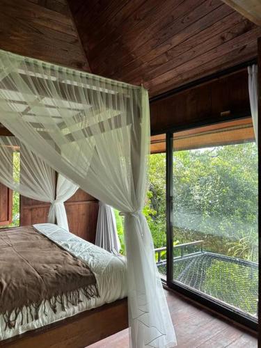 ein Schlafzimmer mit einem Himmelbett und einem großen Fenster in der Unterkunft Karyasari kabin - Tiny House in Blimbing