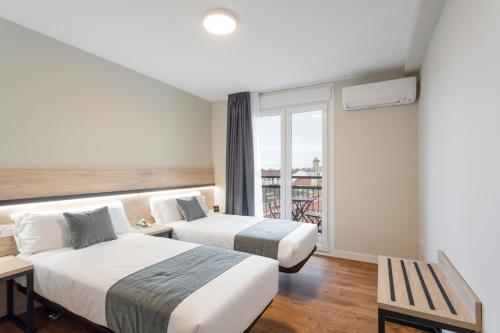 two beds in a hotel room with a window at InsideHome Palencia Catedral in Palencia