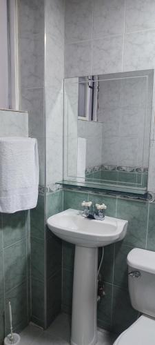 een badkamer met een wastafel, een toilet en een spiegel bij Habitación Versalles in Cali
