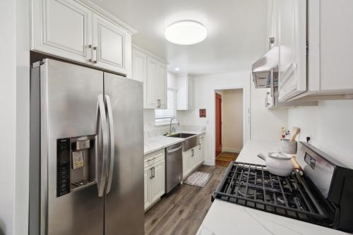a kitchen with white cabinets and a stainless steel refrigerator at Modern Relaxing Retreat with Private Pool home in Azusa