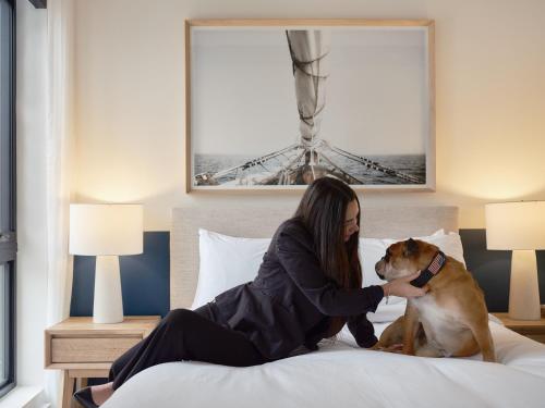 a woman sitting on a bed petting a dog at Hôtel Expérience - Quartier Des Marinas in Magog-Orford