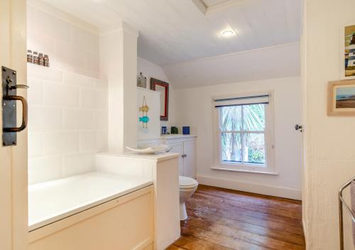 a white bathroom with a toilet and a window at Ball Cottage in Little Petherick