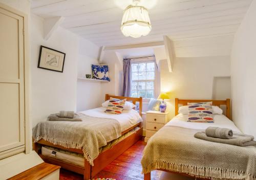 two beds in a bedroom with white walls and wooden floors at Ball Cottage in Little Petherick