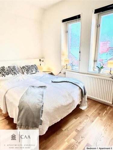 a white bedroom with a bed and two windows at C Apartments Annedal in Gothenburg