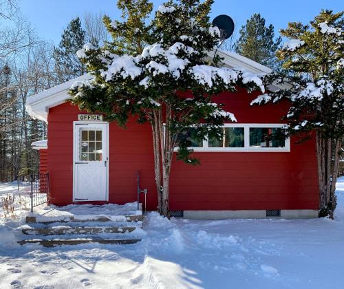 a red house with a white door in the snow at The Lorca Adirondacks Motel in Indian Lake