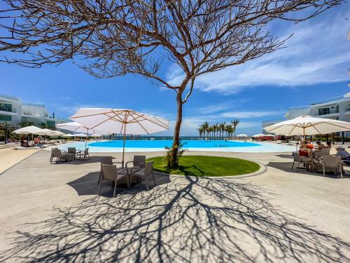 a tree with chairs and umbrellas next to a pool at Aria Ocean View Condo 206 by Kivoya in Nuevo Vallarta 