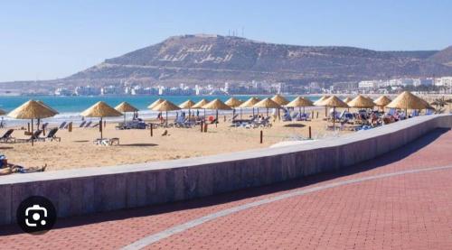 Appartements à AGADIR 10min de la plage في أغادير: شاطئ به مجموعة من المظلات والمحيط