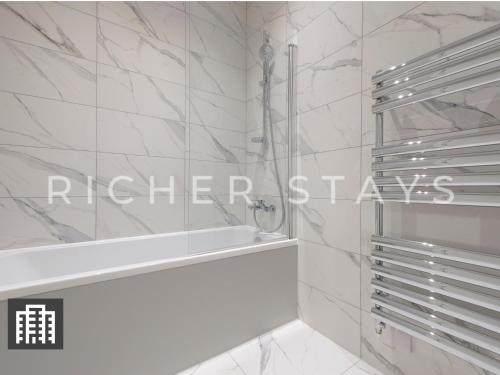 a bathroom with white marble walls and a bath tub at Exquisite 3BR Duplex Period Conversion, Air-con & Amenities in London