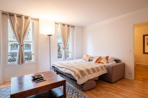 a bedroom with a bed and a table and windows at Cosy & Well-Connected 1BD ApartmentSaint Lazare in Paris