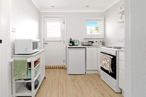 a white kitchen with a microwave and a stove at The Hidden Door Bowral Cottage - The Love of Bowral in Bowral