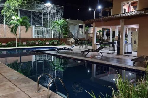 a swimming pool with chairs next to a house at night at Cariri Vivenda - Apto completo com 02 quartos climatizados, estacionamento e portaria 24 horas in Juazeiro do Norte