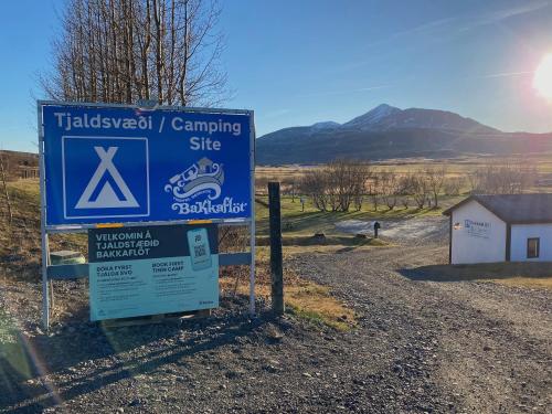a sign for a camping site with mountains in the background at Bakkaflöt Guesthouse in Varmahlid