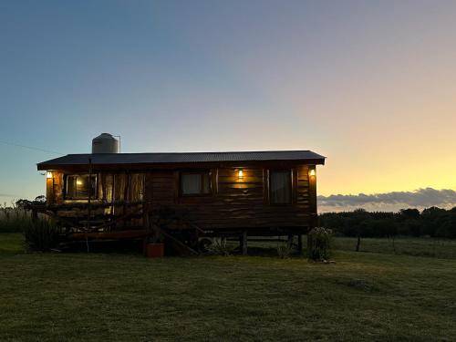 una cabaña de madera con luces encendidas en un campo en Cabaña Guanumby en Tandil