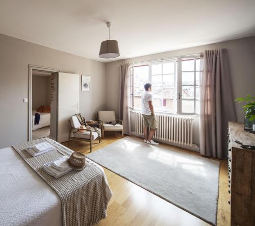 a man standing in a bedroom looking out the window at Villa Caroline - Chambres d'Hôtes in Albi