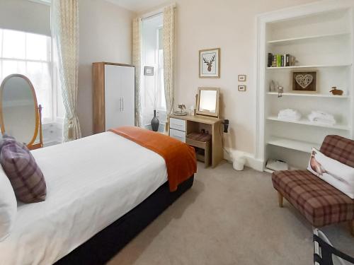 a bedroom with a bed and a chair and a mirror at Flat 3, Barron House in Nairn