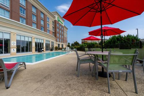 un patio con mesa y sillas con sombrillas rojas en Holiday Inn Murfreesboro, an IHG Hotel, en Murfreesboro