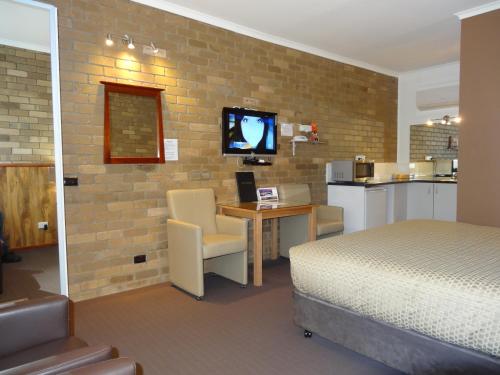 a bedroom with a bed and a desk with a television at Peppinella Motel in Ballarat