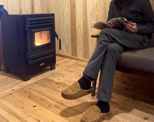 a man sitting on a couch reading a book next to a stove at ビーチまですぐそこ「一軒家貸切ミチカケ」 in Meitsu