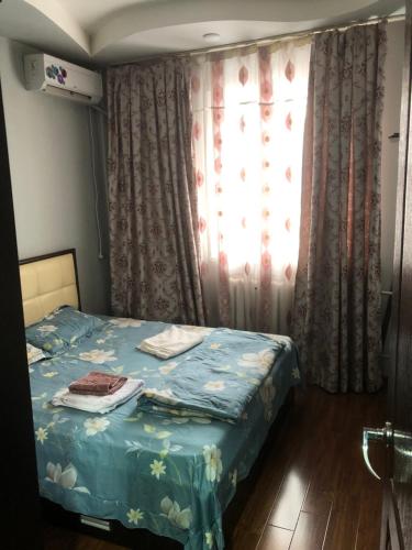 um quarto com uma cama com um cobertor azul e uma janela em Айбек 20 em Yakkasaray