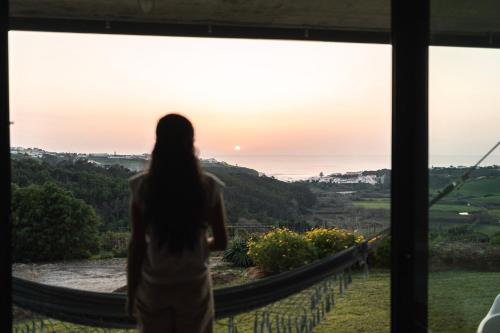 una mujer parada en una hamaca mirando por una ventana al atardecer en Quinta Raposeiros en Santo Isidoro