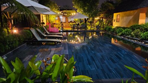 a swimming pool at night with chairs and umbrellas at Phoenix Hotel Pool Villa in Hoi An