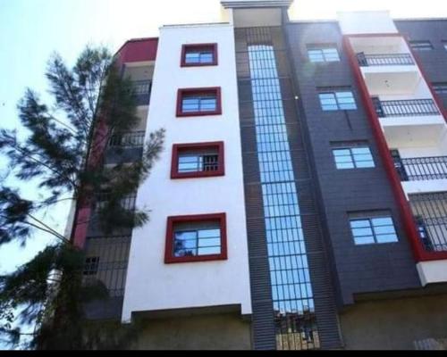 a tall white building with red windows and a tree at NorbertO768976732 in Kisumu