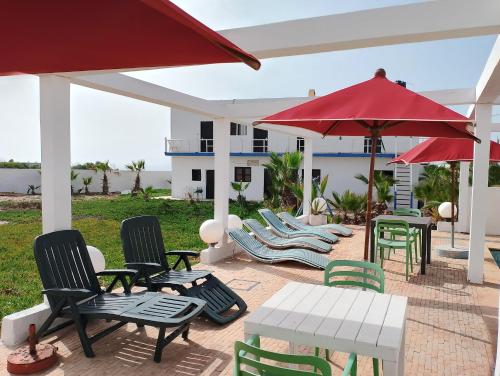 a patio with chairs and tables and a red umbrella at Riad & Restaurant Ocean Beach Douira in Agadir
