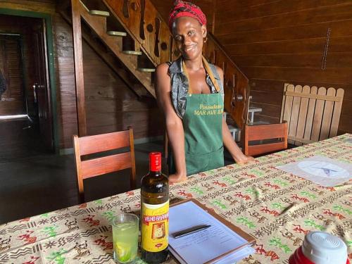 une femme debout à côté d'une table avec une bouteille d'alcool dans l'établissement Pousadinha Mar Ave Ilha, à Principe