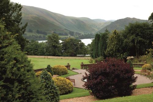 a garden with benches and trees and mountains in the background at Macdonald Leeming House in Watermillock