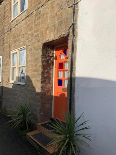 an orange door on a brick building with two plants at Bell Cottage in Bridport