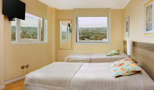 two beds in a room with two windows at Hotel Aranjuez in Chillán