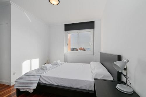 a white bedroom with a large bed and a window at Moderno piso en el corazón de Baiona by CABANA Rentals in Baiona
