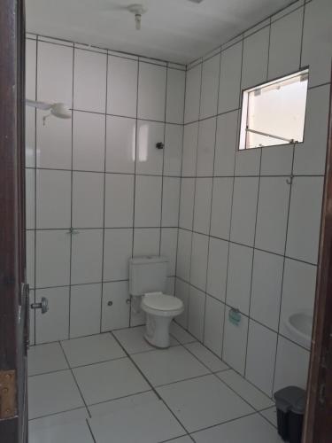 ein weiß gefliestes Bad mit einem WC und einem Fenster in der Unterkunft Sitio in Itapoa