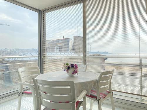 une table blanche avec des chaises blanches et un vase avec des fleurs dans l'établissement 507-Bel appartement en bordure de la plage d'Erquy, à Erquy