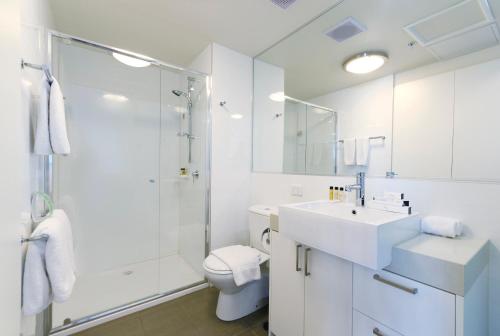 a white bathroom with a shower and a sink and a toilet at Fraser Place Melbourne in Melbourne